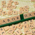 Scrabble tiles forming the phrase "Labor Day" on a green surface, symbolizing the holiday.