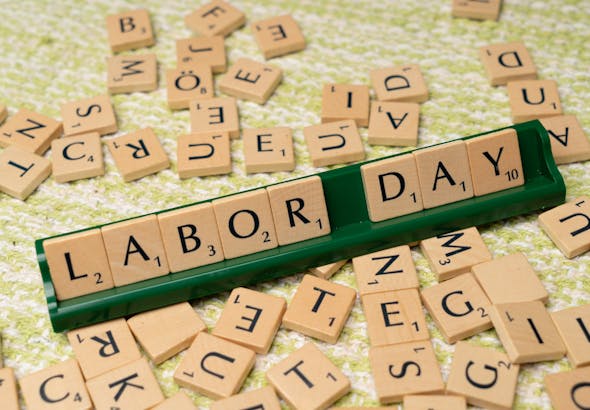 Scrabble tiles forming the phrase "Labor Day" on a green surface, symbolizing the holiday.