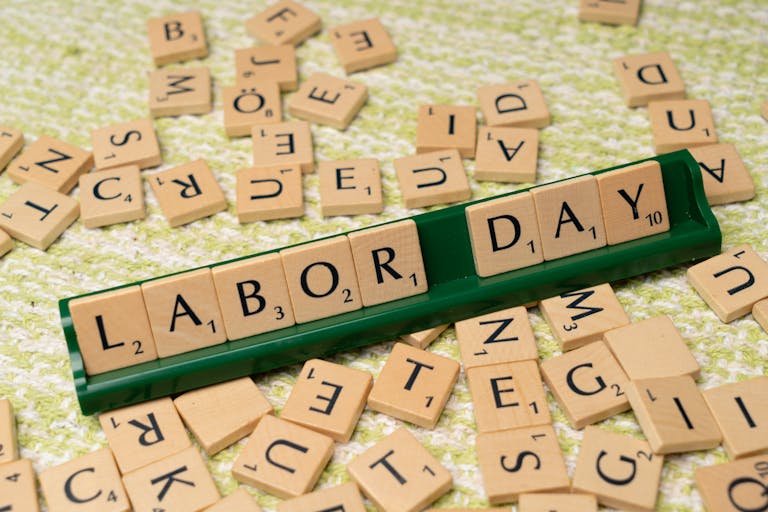 Scrabble tiles forming the phrase "Labor Day" on a green surface, symbolizing the holiday.